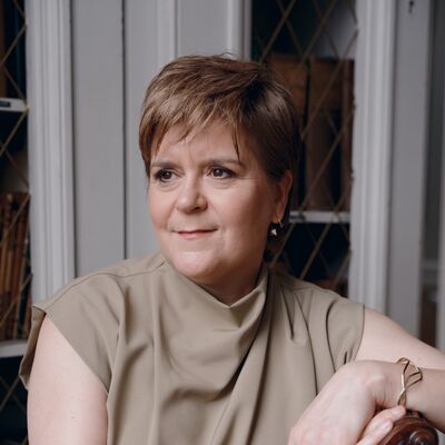 Nicola Sturgeon wearing a beige top leaning on the back of a chair.