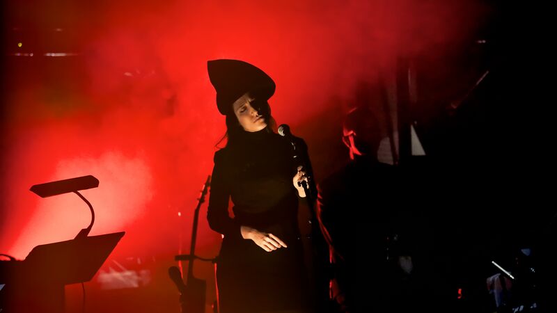 A woman dressed in black wearing a pointed hat holding a mic