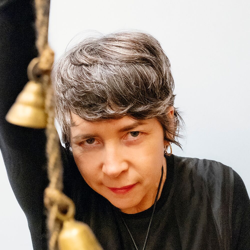 Person with short dark hair holding bells and looking into the camera