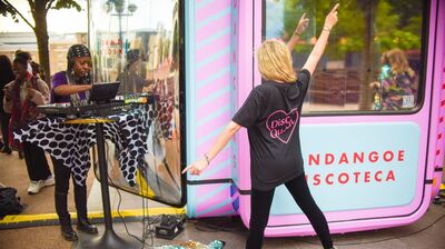 A dancer with her arms up in the air infront of a disco box and a DJ