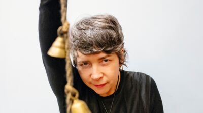 Person with short dark hair holding bells and looking into the camera