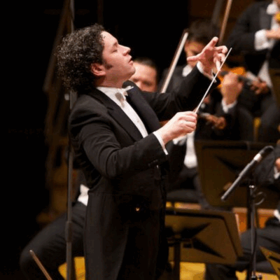Gustavo Dudamel conducting an orchestra wearing a black suit.