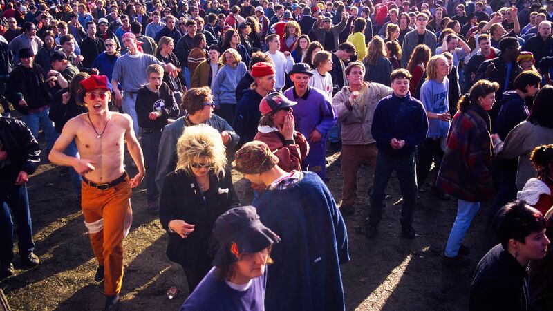 Large crowd of people at festival wearing colourful outfits with white tents in the background