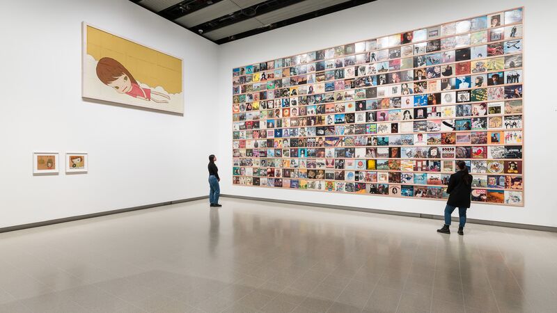 Two people in a large exhibition space looking at a collection of records displayed on one wall