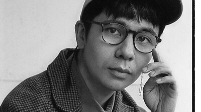 Black and white image of Ocean Vuong wearing a cap and a check jacket.