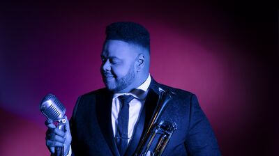 A person wearing a suit jacket and tie holding a trumpet and silver microphone