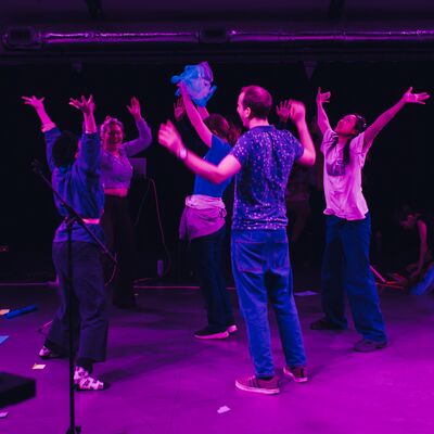 Group of people in a room dancing with their arms in the air lit in purple lighting