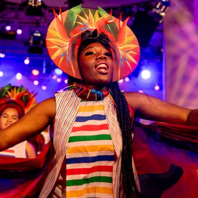 A woman wearing a colourful head piece dancing