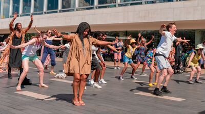Members of an audience all dance in the sunshine lifting their arms and smiling