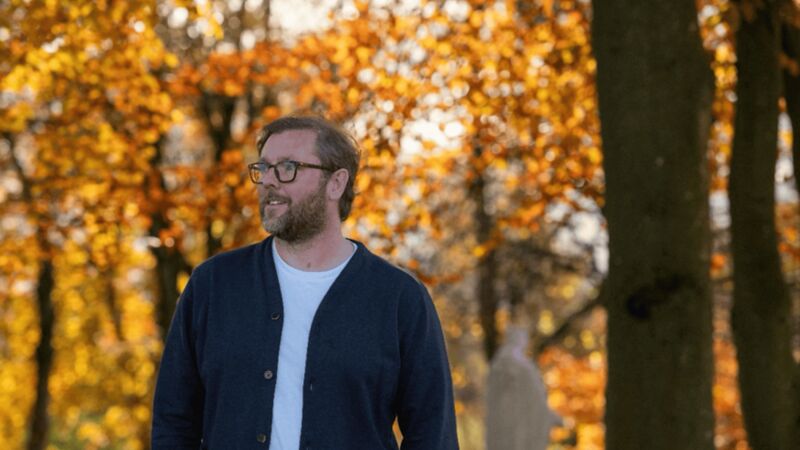 Damian Barr surrounded by autumn trees.