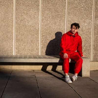 An orchestra conductor dramatically moving their arms onstage in front of seated musicians and an audience behind