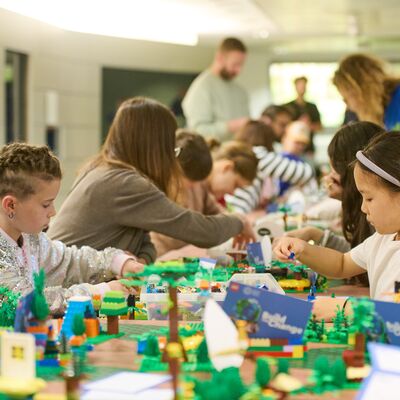 Group of children and adults sitting around a long table playing and building with LEGO