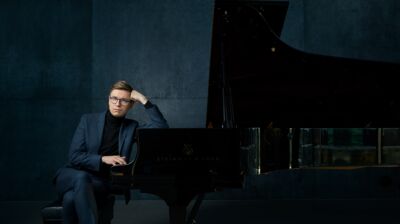 Pianist Vikingur Olaffson in a navy blue suit leaning on a grand piano