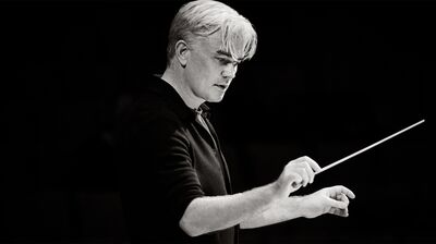 Black and white portrait of LPO's Principal Conductor holding a baton looking down with arms at 90 degree angles