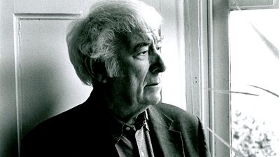 Black and white photo of a man wearing a shirt and blazer, against the feint light peaking through a window.