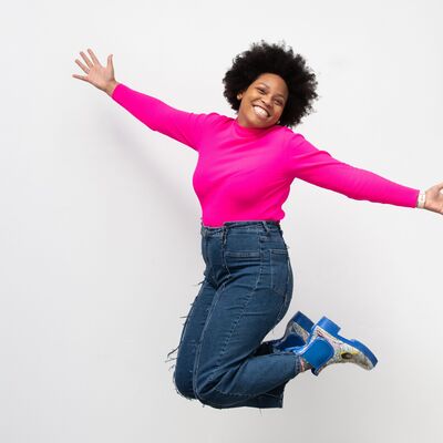 Someone wearing a bright pink top and blue jeans, jumping in the air with arms outstretched