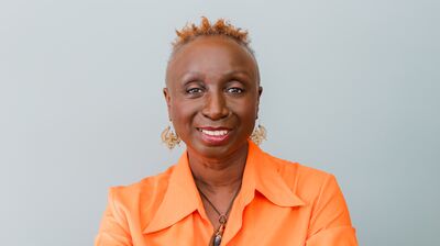 Lisa Smith a woman smiling whilst wearing an orange shirt sitting at a wooden table with short ginger hair.