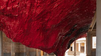 Large red textured sculpture hanging down from the ceiling to the floor in a space with stone floors and pillars