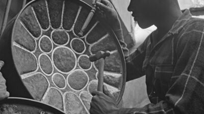 Black and white image of a man hammering a steel pan drum into shape