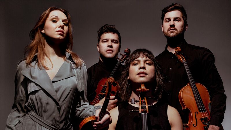 A string quartet holding their violins, wearing neutral clothing