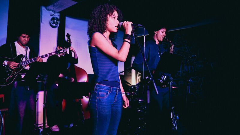 Musicians on stage performing with someone in red singing in to a microphone