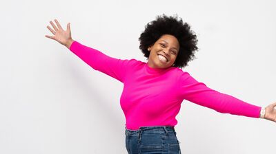 Someone wearing a bright pink top and blue jeans, jumping in the air with arms outstretched