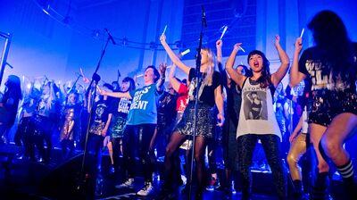 Group of people singing an dancing on stage in a blue room