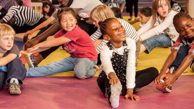A group of young children are having fun together, doing stretches and poses on the floor.