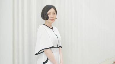 A woman wearing a white dress against a white background, she has short dark hair