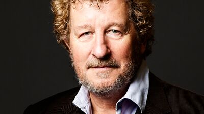 Sebastian Faulks, wearing a black blazer and shirt, looks directorly into the camera with short curly hair.