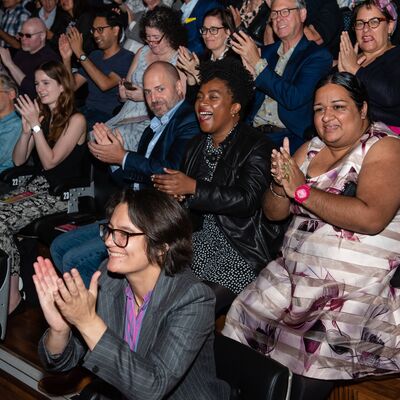 Seated audience members clapping at an event with joy on their faces.