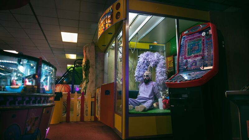 A person with blonde hair and wearing a blue outfit sitting on stacked chairs in a blue/grey room.