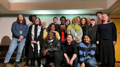 Sixteen people pose for a photo, some crouching and others standing and all smiling