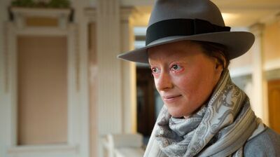 Rachael Boast wearing a grey hat and scarf whilst facing and looking left off camera.