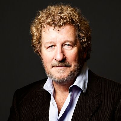 Sebastian Faulks, wearing a black blazer and shirt, looks directorly into the camera with short curly hair.