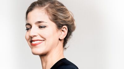 Smiling headshot of a woman with light brown hair tied up looking down to the left