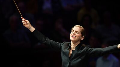 Karina Canellakis spreading her arms joyfully with eyes closed and a conductors baton in hand