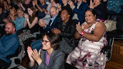 Seated audience members clapping at an event with joy on their faces.