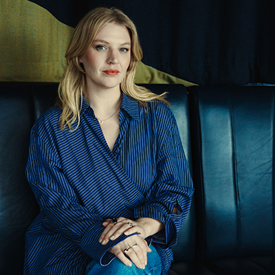 Singer Self Esteem, a young woman with long blond hair, sits on a leather sofa seat