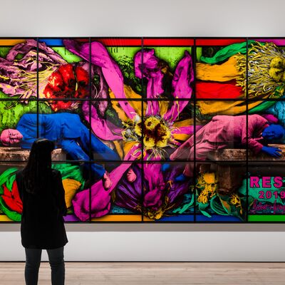 A person looking at a large and colourful artwork with black grid lines overlaying it, hanging on a white wall