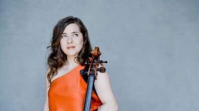 A woman in an orange dress, posing with a cello