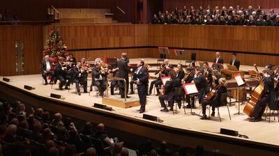 Orchestra performing on large wooden stage with a choir behind on a higher platform at the Royal Festival Hall