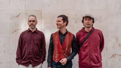 Three mean wearing red shirts, standing against a pale marble wall