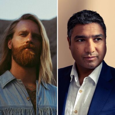 Sam Ryder who has long blonde hair and wears a blue shirt & Nick Mohammed with short dark hair, wearing a suit and white shirt