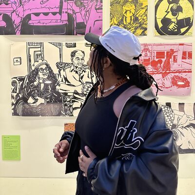 Artist Olivia Twist stands with her profile to camera looking at a wall of her artwork.