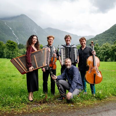 A group of musicians posing in a green valley, with a waterfall in the background