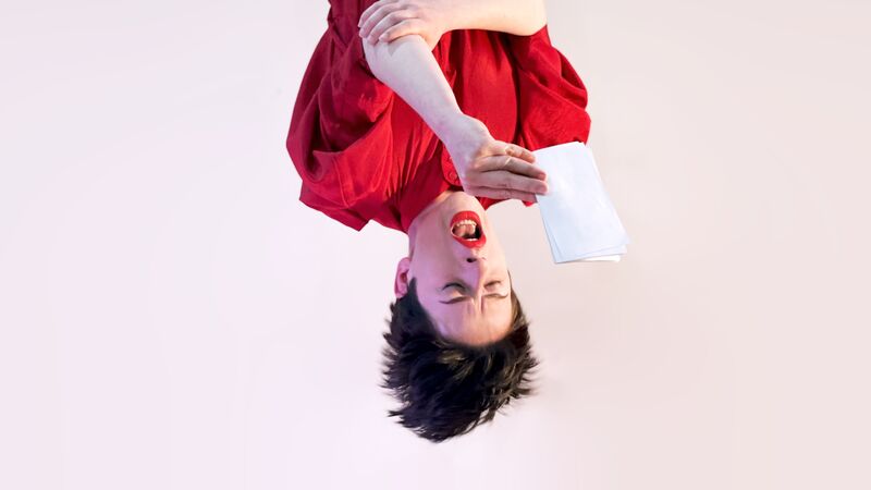 An upside down person with their hanging off their head reads off a small piece of white paper.