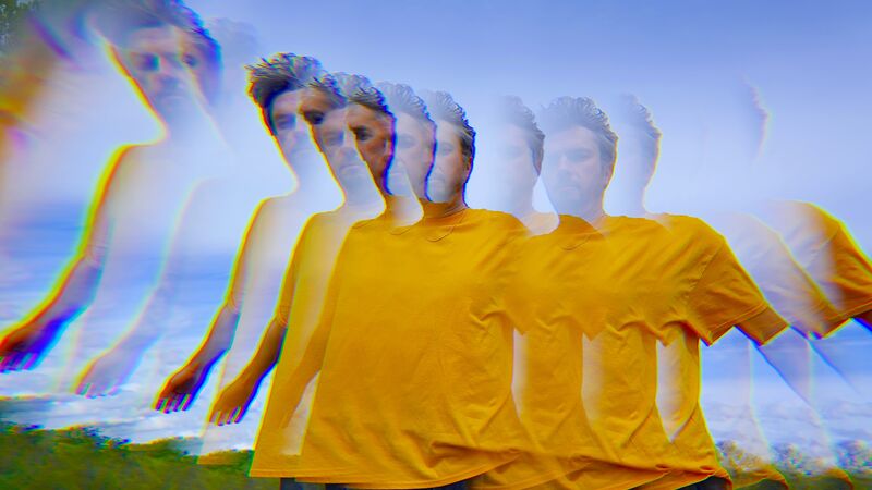 Blurry and refracted image of Tom Skinner wearing a yellow t-shirt