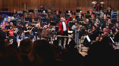 An orchestra performing wearing Christmas clothing including red jackets, santa hats and tinsel