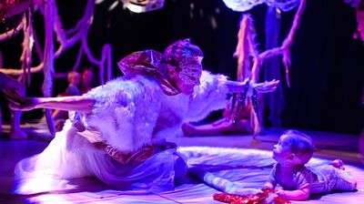 A performer kneeling on the floor wearing a mask, with a baby watching them